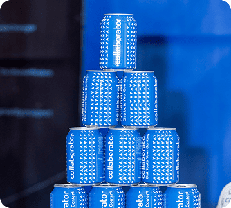 Pyramide de canettes bleues de la marque Collaborator empilées sur plusieurs niveaux, créant un affichage accrocheur contre un fond bleu